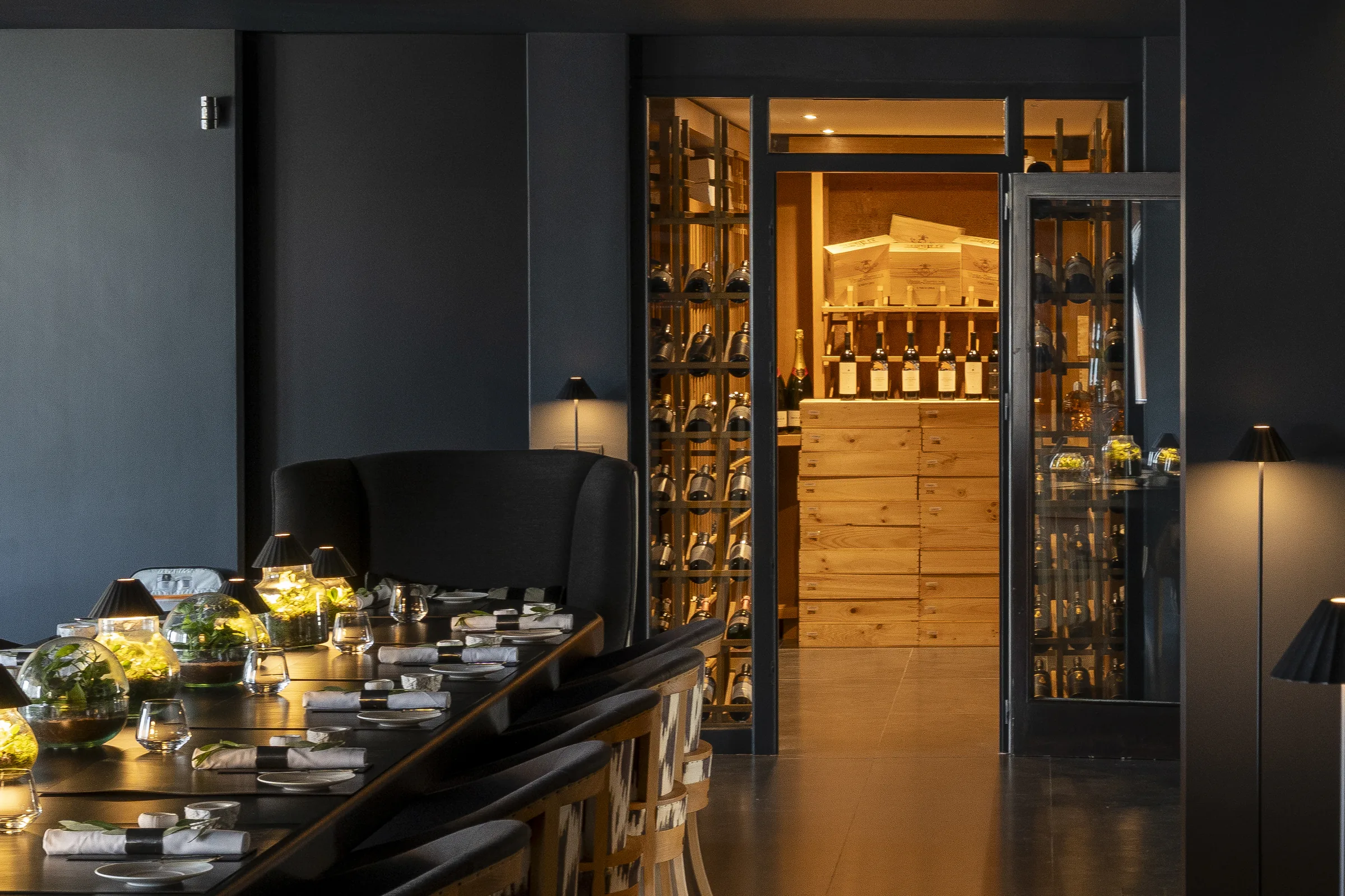 The dining table with the illuminated wine cellar visible through glass doors
