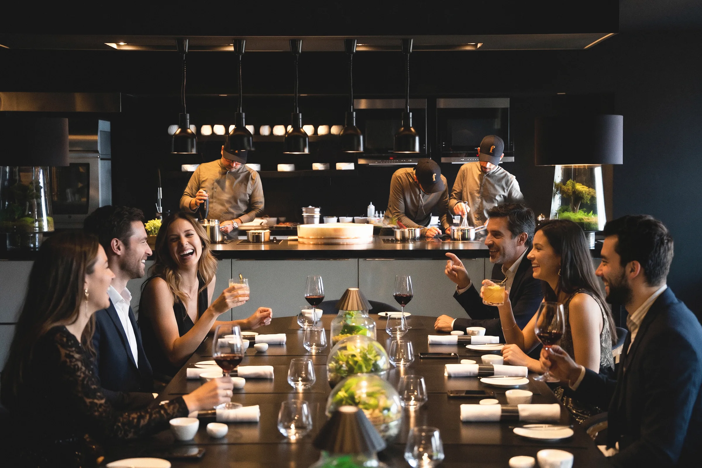 Guests laughing at the Chef's Table while chefs prepare courses in the open kitchen