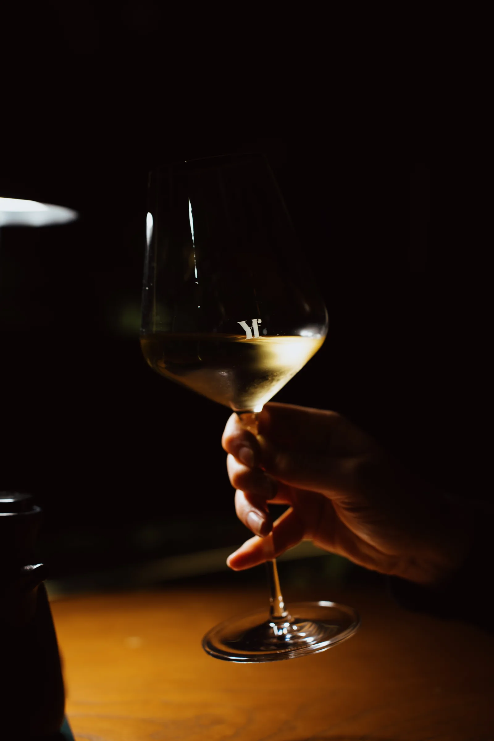 A hand holding a glass of white wine in warm candlelight